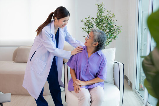 Doctor assisting her old patient at nursing home. Caregiver helping senior patient sit on sofa. Friendly Doctor talking with patient at nursing home