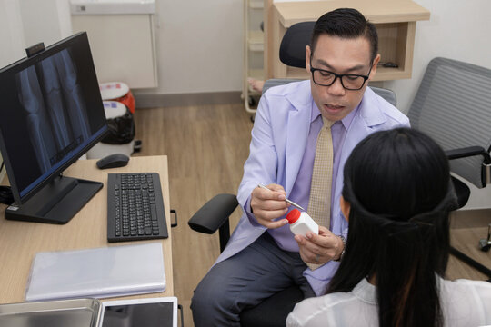 male doctor in a white coat explaining medication and prescription details to a female patient in a modern clinic office, pointing at a medicine bottle.