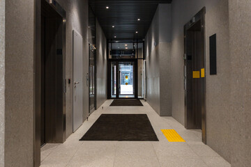 Elevator lobby of modern apartment building with stone walls and glass exit door to courtyard. Interior hallway with lifts. Residential architecture. Entrance hall and access concept. © Анастасия Бурлакова