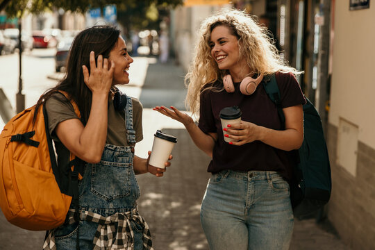 Young friends walking urban street, sharing coffee and laughing