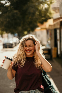 Young woman smiling enjoying music and coffee outdoors