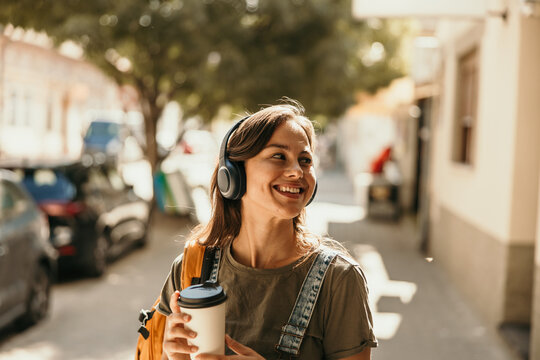 Woman listening to music walking urban street with coffee