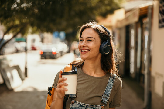 Happy woman enjoying music and coffee in city