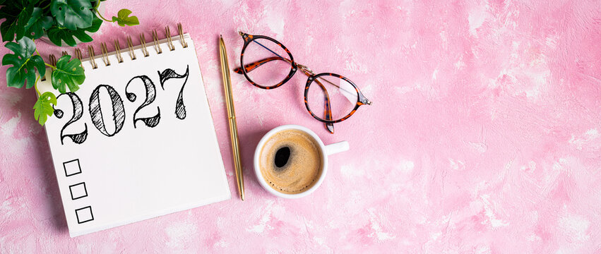 New year resolutions 2027 on desk. 2027 resolutions list with notebook, coffee cup on pink table. Goals, resolutions, plan, action, checklist concept. New Year 2027 template, copy space