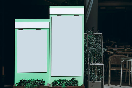 Two blank vertical menu panels mounted on mint green freestanding displays outside a restaurant, offering realistic templates for food branding, specials or promotions