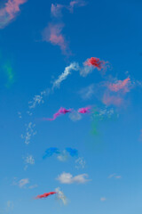 Colored smoke trails drift across a blue sky during an aerial performance. Airshow spectacle represents motion, celebration, visual impact and aviation entertainment. © Natallia