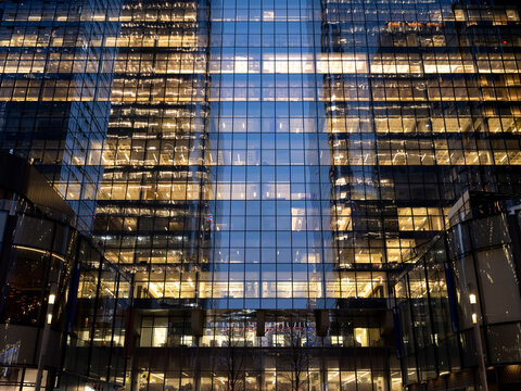 Wide low-angle view of glass-clad business office towers in Midtown Manhattan at dusk, their illuminated interior floors visible through the curtain wall facade. 