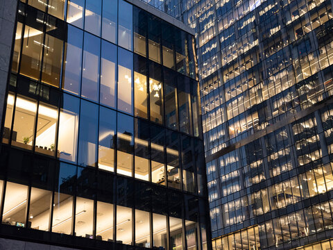 Low-angle view of glass-clad business office towers at Hudson Yards in Midtown Manhattan at dusk, with illuminated interior offices visible across multiple stories. 