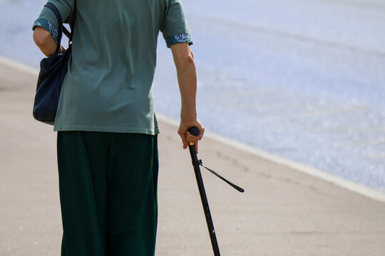 Woman in muted green attire walks along seaside promenade holding cane