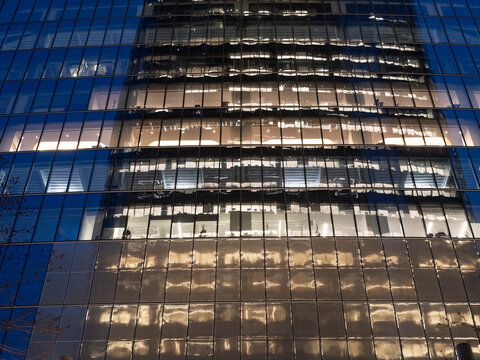 Low-angle view of a business office tower in Manhattan at night, its glass curtain wall revealing illuminated interior offices in horizontal bands. 