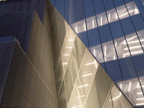 Low-angle view of a museum building's angular exterior in Manhattan at dusk, with folded mesh cladding panels and an illuminated glass facade.