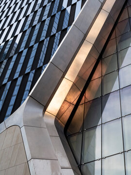 Low-angle view of a curved, sculptural building facade in Manhattan, combining smooth stone-clad ribs with a bolted glass curtain wall. 