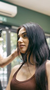 Professional hairstylist using a hairdryer and a round brush to style a beautiful client's long dark hair in a modern beauty salon. Vertical
