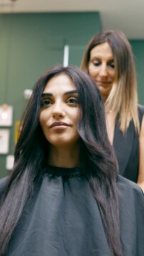 Beautiful smiling customer getting her hair styled by a professional female hairdresser in a modern beauty salon after a haircut. Vertical