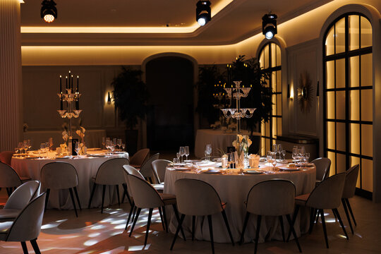 Elegant dining hall with warmly lit tables, white tablecloths, candles, and flowers, creating a sophisticated atmosphere for a luxurious event or celebration