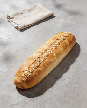 Slender golden Easter bread with sesame seeds along the ridge on a stone surface with linen napkin.