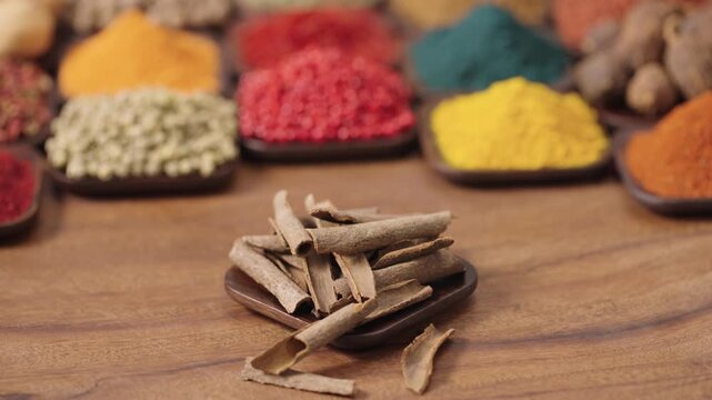 chinese cassia cinnamon bark in a square bowl on a wooden table, surrounded by various spices and herbs.