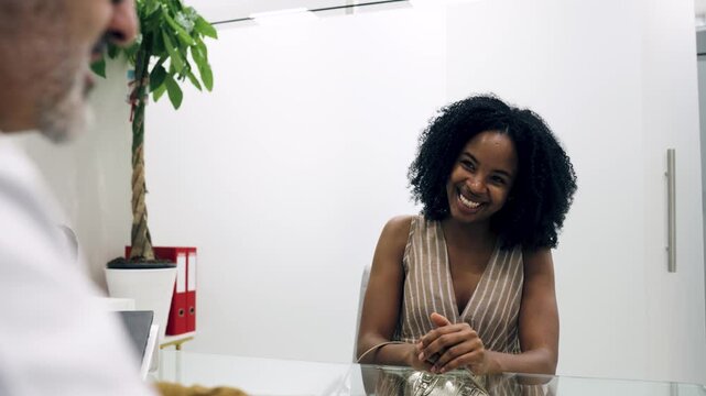 Young professional African American woman sitting at a desk and positively talking with a male recruiter during a job interview in an office