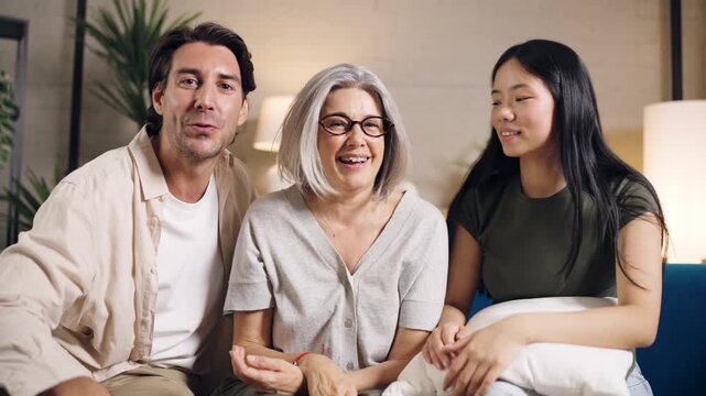 Happy diverse family members communicating online from home. An older mother with her adult son and asian daughter in law sitting on couch