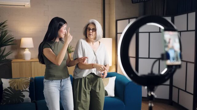 Multiethnic young and senior women recording a dancing video for a social network. Happy bloggers creating content using a ring light at home