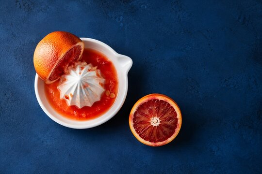 Blood orange halves with a ceramic citrus juicer on a blue background