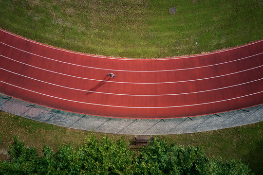 Person running on red stadium track, top view