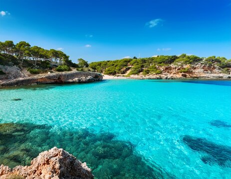 crystal clear turquoise water at cala agulla beach with rocks and hillside coastline in mallorca