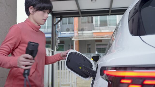 Woman unplugs the charging cable of an electric vehicle (EV car), Sustainable clean energy