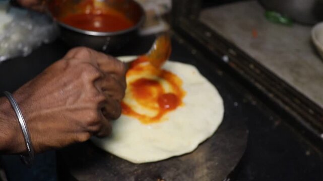 Close up of a professional chef spreading fresh tomato sauce with a ladle on a raw pizza dough, the first step in preparing a delicious homemade traditional italian margherita.