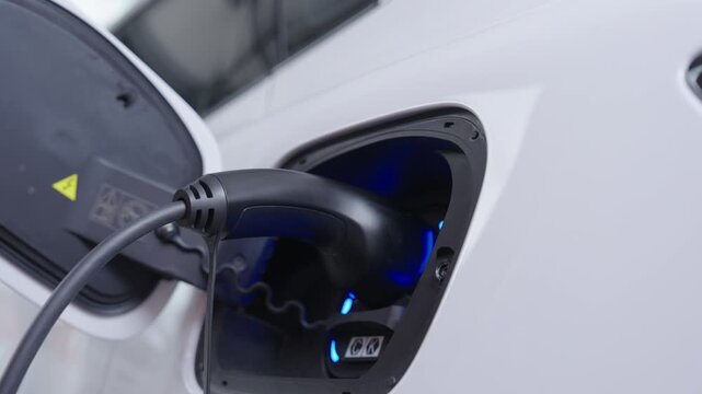 Hand of woman plugs the charging cable of an electric vehicle (EV car), Sustainable clean energy