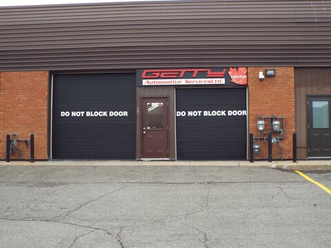 Gloucester, Ontario, Canada &ndash; July 19, 2026: "Getty Automotive Services Ltd." shop exterior features two black garage doors with warning text and a central entrance door at 5340 Canotek Rd.