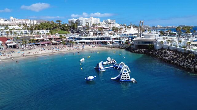 &Oacute;rbita a&eacute;rea de una bah&iacute;a de arena tranquila con parque acu&aacute;tico hinchable flotante, paseo mar&iacute;timo y hoteles, Costa Adeje, Tenerife, Espa&ntilde;a