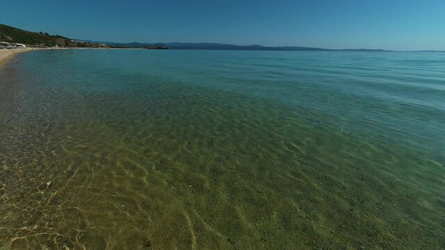 Clear waves lap a sunlit shore. Trani Ammouda, Greece