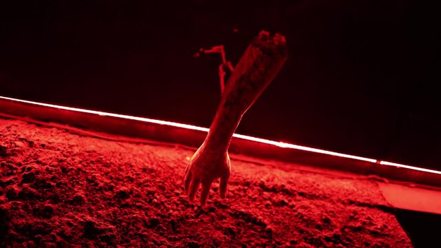 Halloween horror decor with a severed arm hanging from the ceiling under intense red light creating a gruesome haunted house scene filled with fear and dark suspense dread