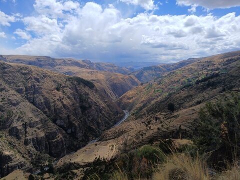Valley with a distant river, mountains, forest, and a cloudy sky in the background in Surimana, Cusco, Peru.