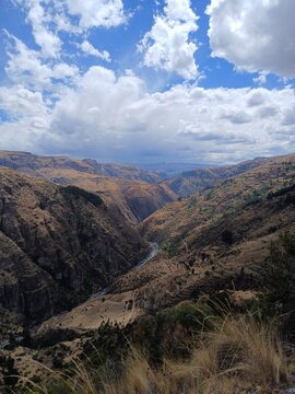 Valley with a distant river, mountains, forest, and a cloudy sky in the background in Surimana, Cusco, Peru.