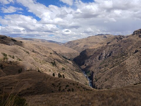 Valley with a distant river, mountains, forest, and a cloudy sky in the background in Surimana, Cusco, Peru.
