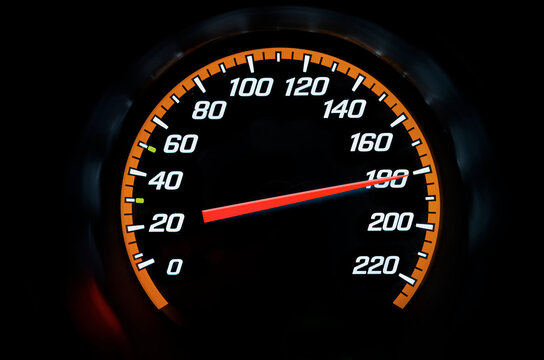 A illuminated car speedometer displaying high speed on a dark dashboard.