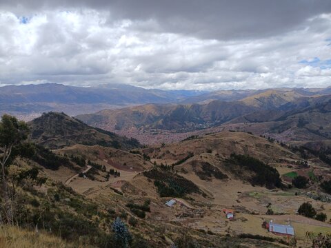 View of mountains and the city in the background under a cloudy sky, with trees in Cusco, Peru.