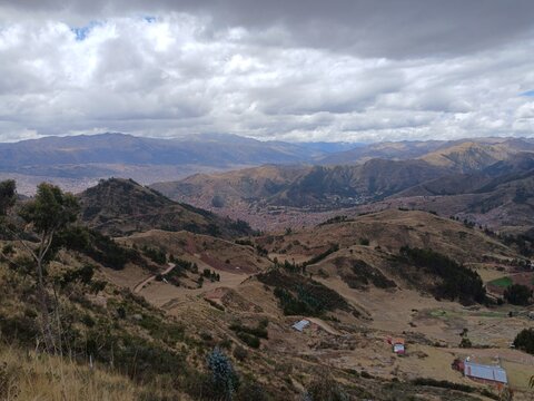 View of mountains and the city in the background under a cloudy sky, with trees in Cusco, Peru.