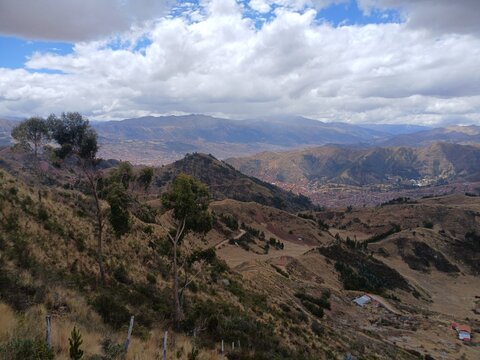 View of mountains and the city in the background under a cloudy sky, with trees in Cusco, Peru.