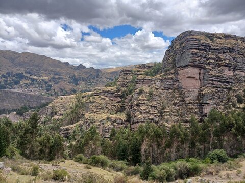 View of a forest and a distant rocky mountain under a cloudy sky in Cusco, Peru.