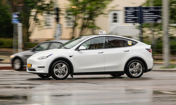Gothenburg, Sweden - July 28 2026: White Tesla Model Y taxi moving through rainy urban traffic.