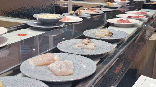 Conveyor belt hotpot buffet with fresh meat seafood and ingredients served on small plates in Asian restaurant
