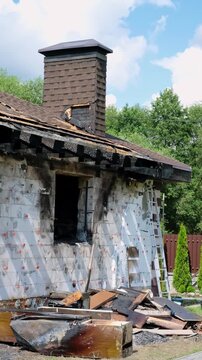 Damaged brick chimney stands on the roof of burned house. Concept of fire insurance. Arson case. Consequences of a gas or battery explosion. Home maintenance, structural repair, building inspection.