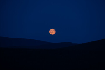 A full moon rising above the silhouette of mountain ridges in the Jizera Mountains. © Jan