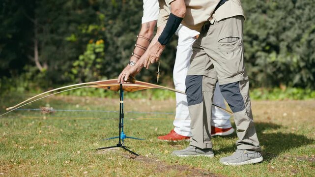 Senior archer putting down his traditional wooden longbow on a stand after a training session in a green field on a sunny summer day