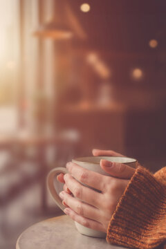 Hands Wrapped Around Ceramic Mug in Cozy Autumn Sweater, Warm Cafe Atmosphere