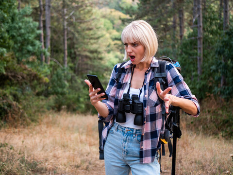 Lost woman hiker looking at smartphone while walking through a forest, feeling panic and uncertainty during her outdoor exploration.