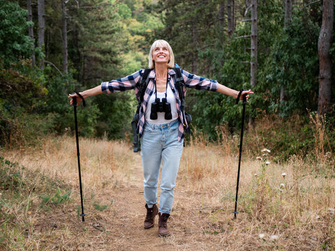 Woman hiker hiking through forest with arms outstretched holding hiking poles, smiling and enjoying nature, freedom, adventure and active healthy lifestyle.